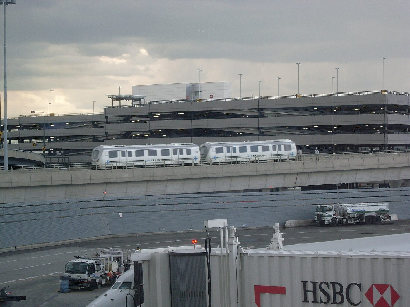Rame de l'AirTrain JFK sur son viaduc devant un parking, vue depuis le terminal 4