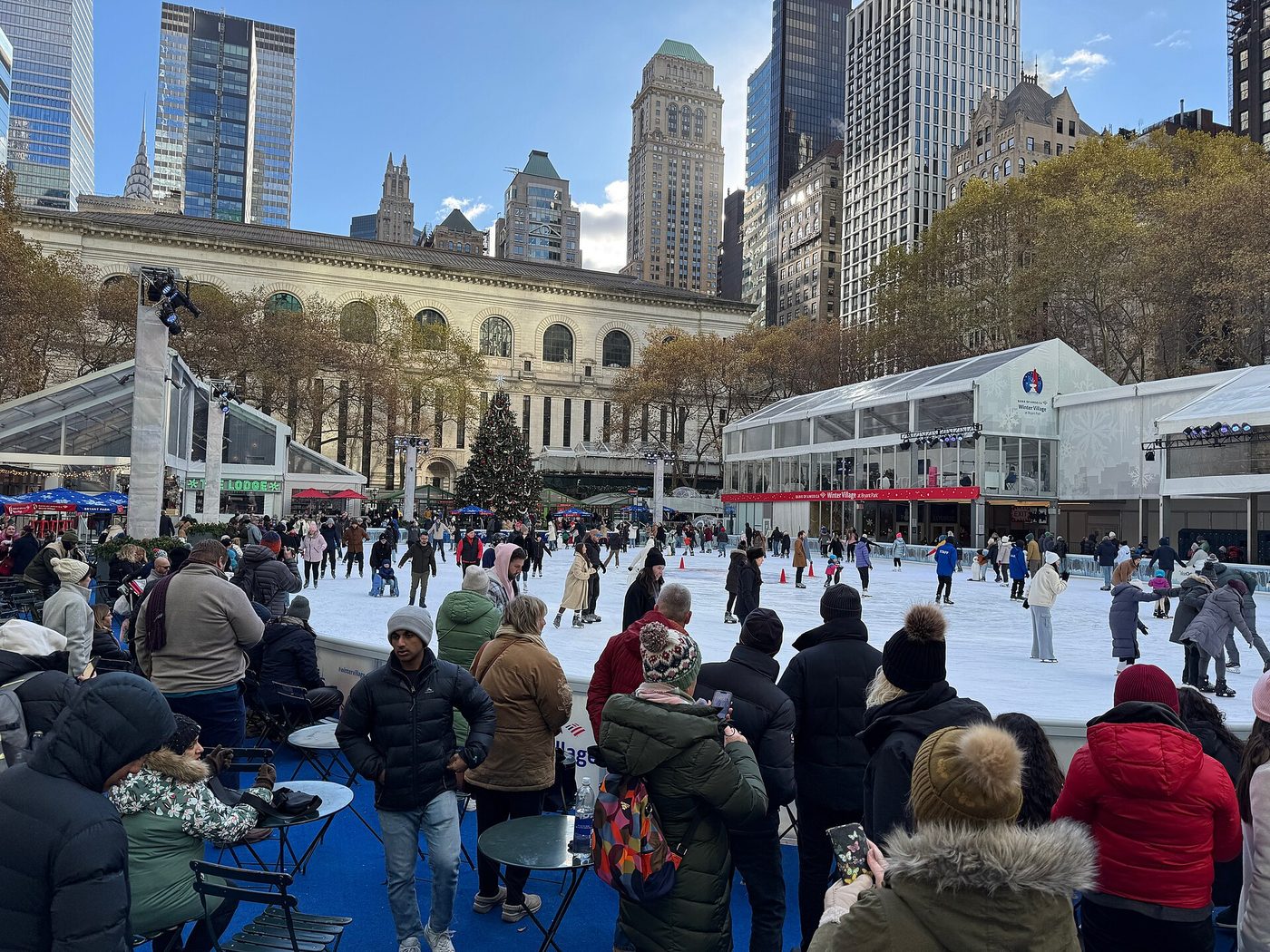 Patineurs sur la glace du Winter Village de Bryant Park, avec la façade de la bibliothèque et les tours de Midtown