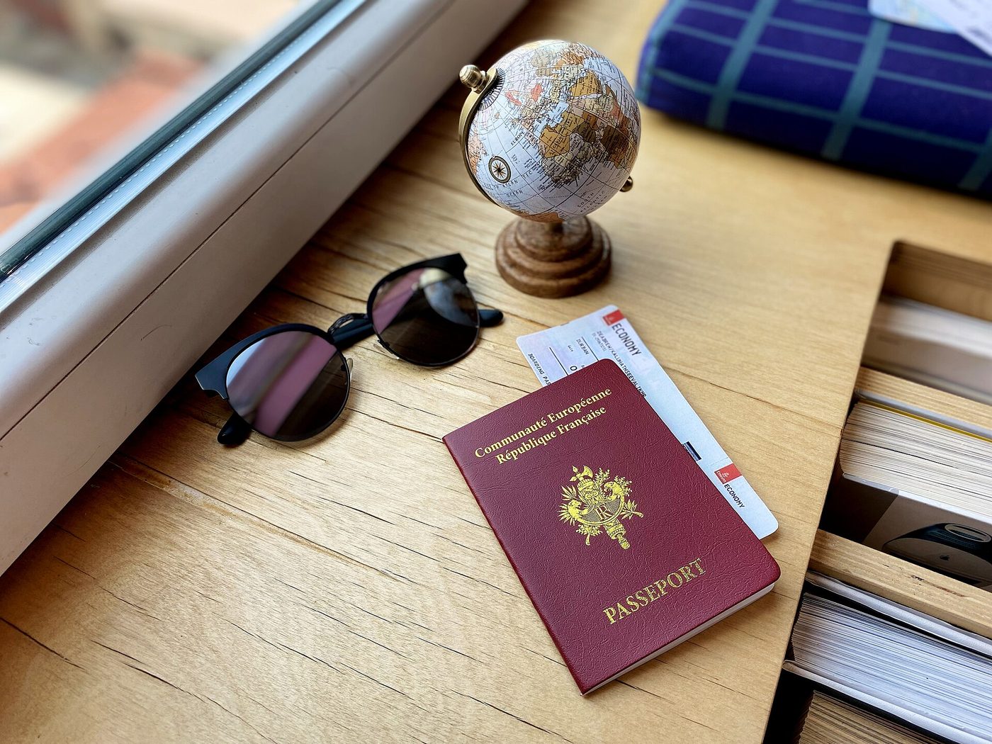 Passeport français posé sur une table avec une carte d'embarquement, des lunettes de soleil et un petit globe