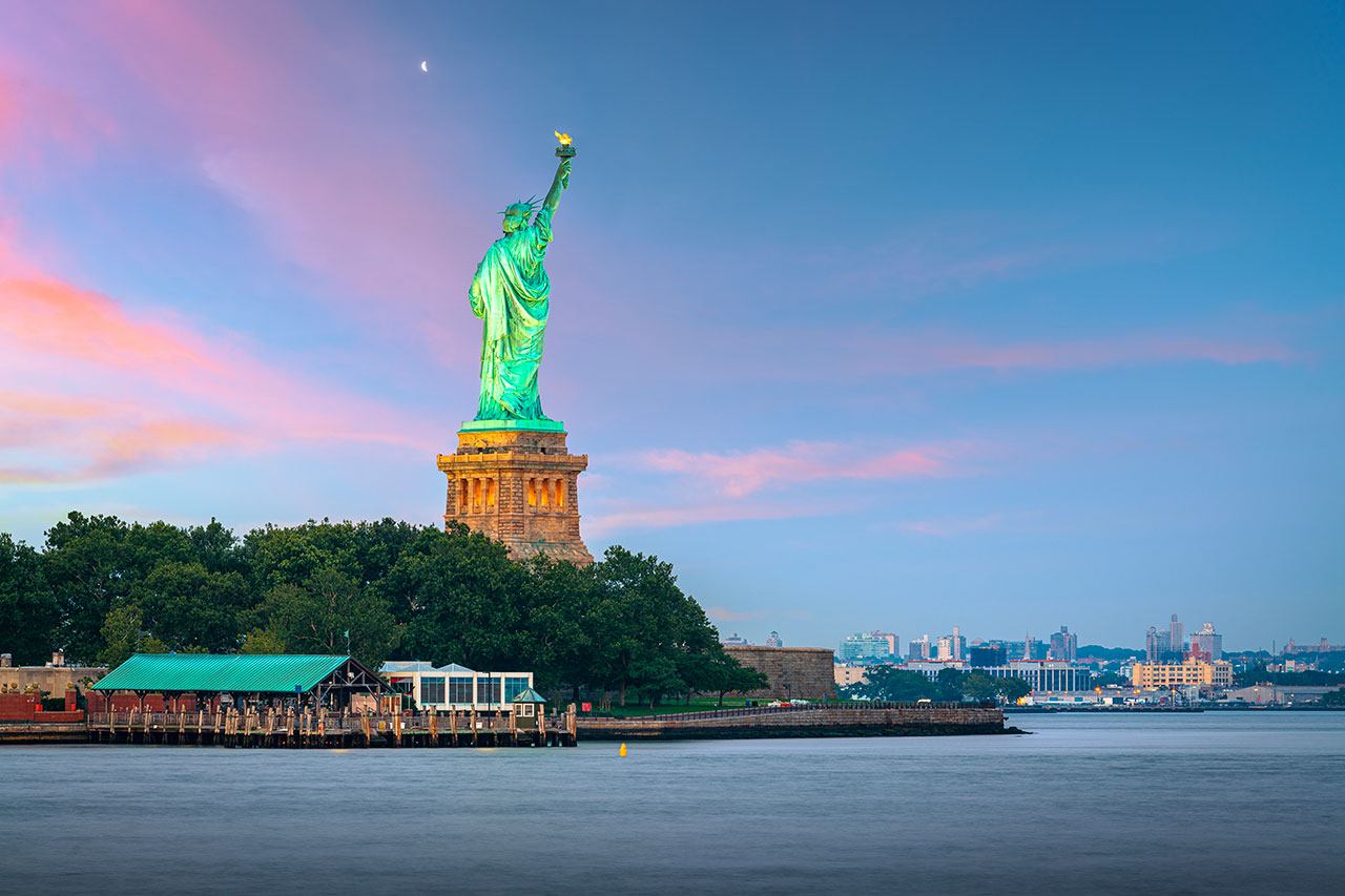 La statue de la Liberté sur Liberty Island au coucher du soleil, vue depuis la baie de New York